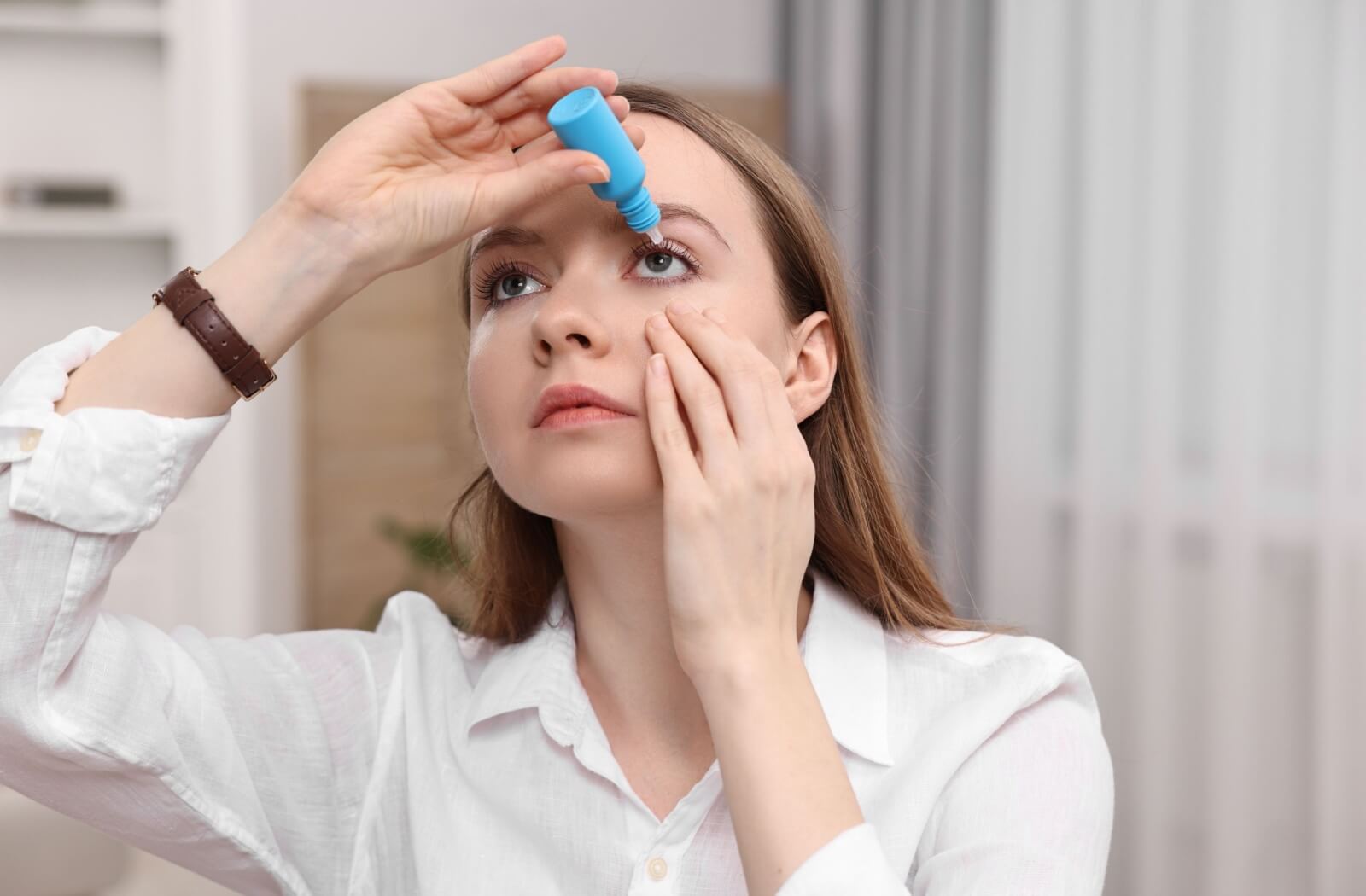 A young adult applies eye drops into their left eye.