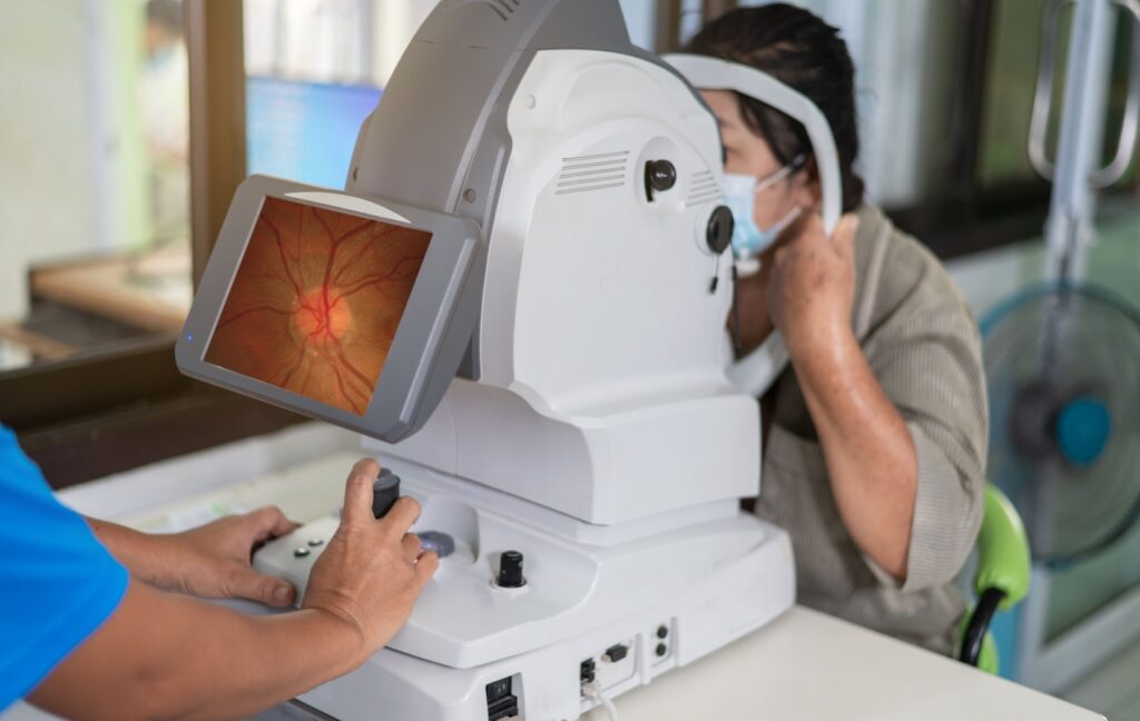 During an eye exam, an optometrist uses a retinal camera to examine their patients' eyes for signs of diabetes.