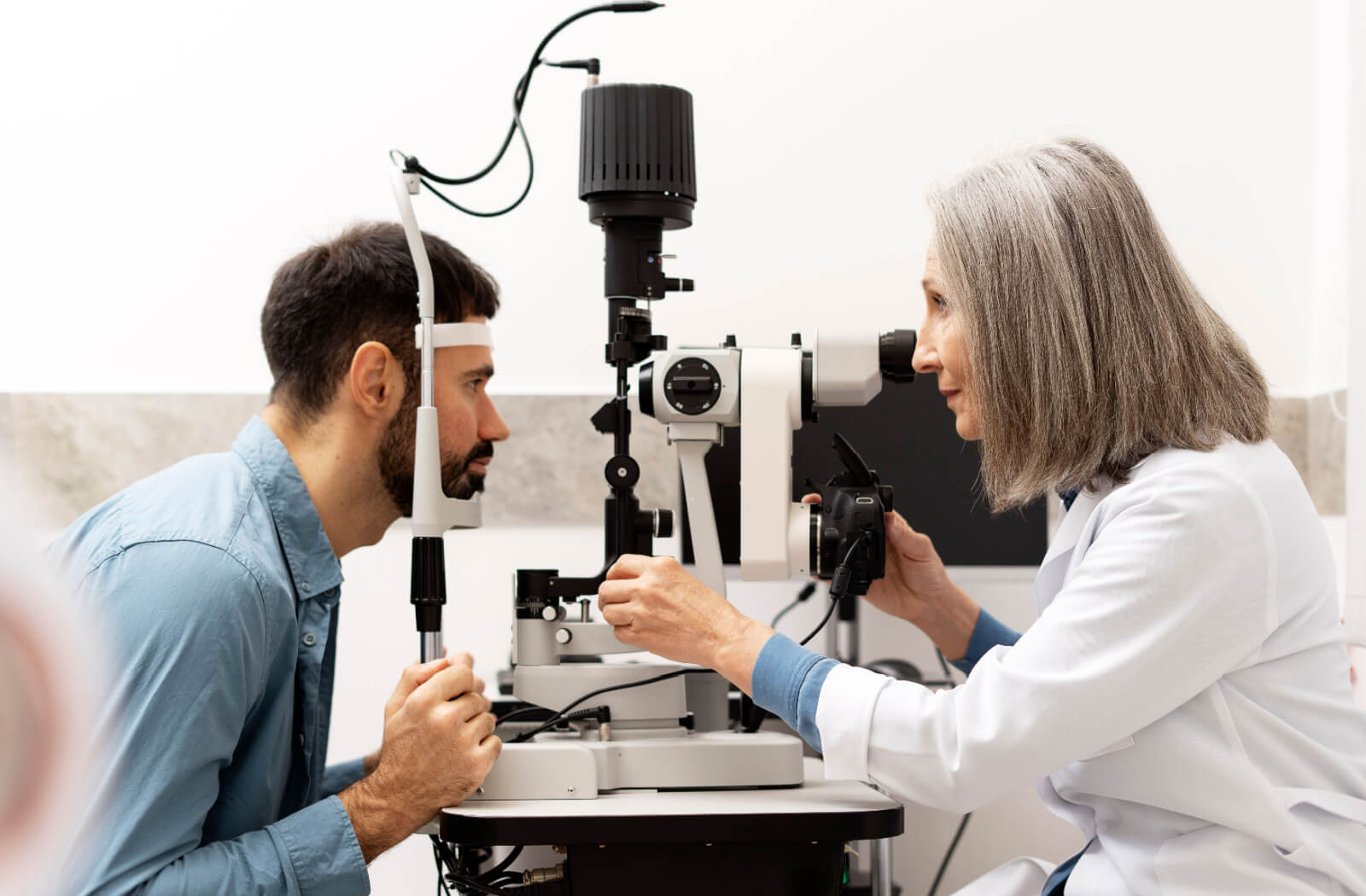 An optometrist carefully examining a patient's eyes during an eye exam to find what's causing their discomfort while blinking.
