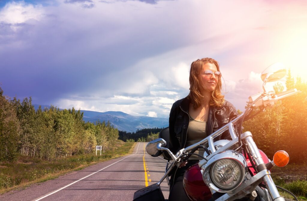 An adult wearing sunglasses pauses a motorcycle ride to take in the gorgeous view of Yukon while doing a cross-country ride