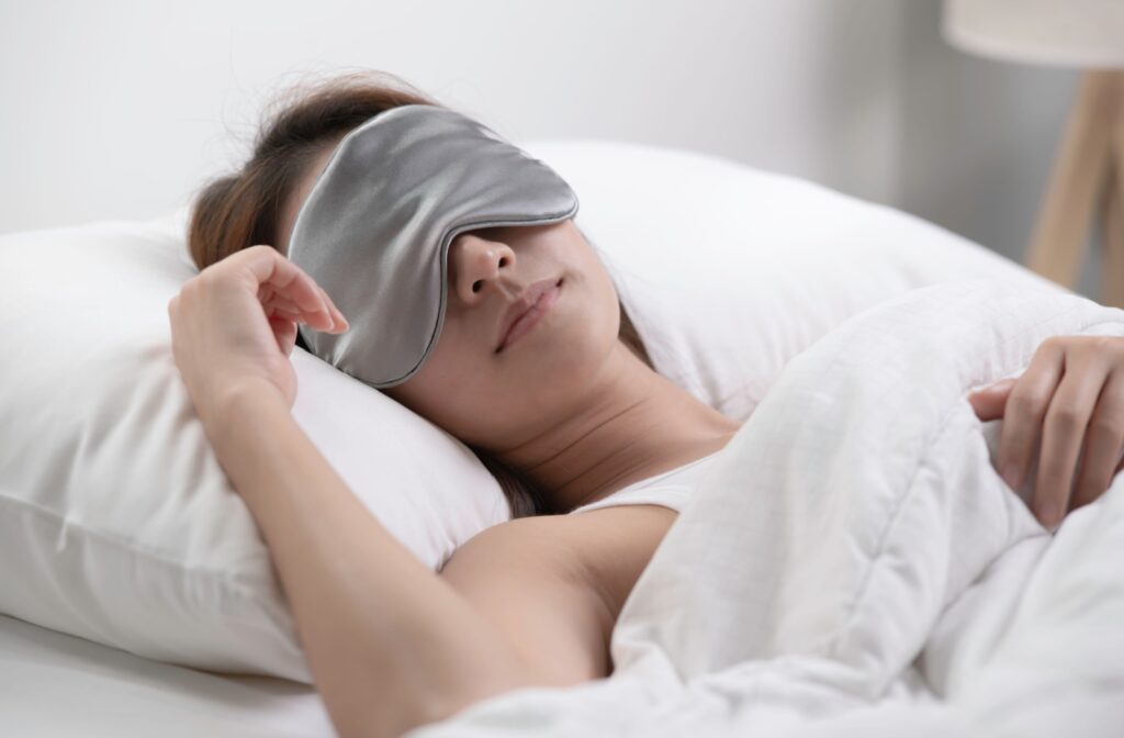 An adult lying in bed with a smile while wearing an eye mask to help with dry eyes.