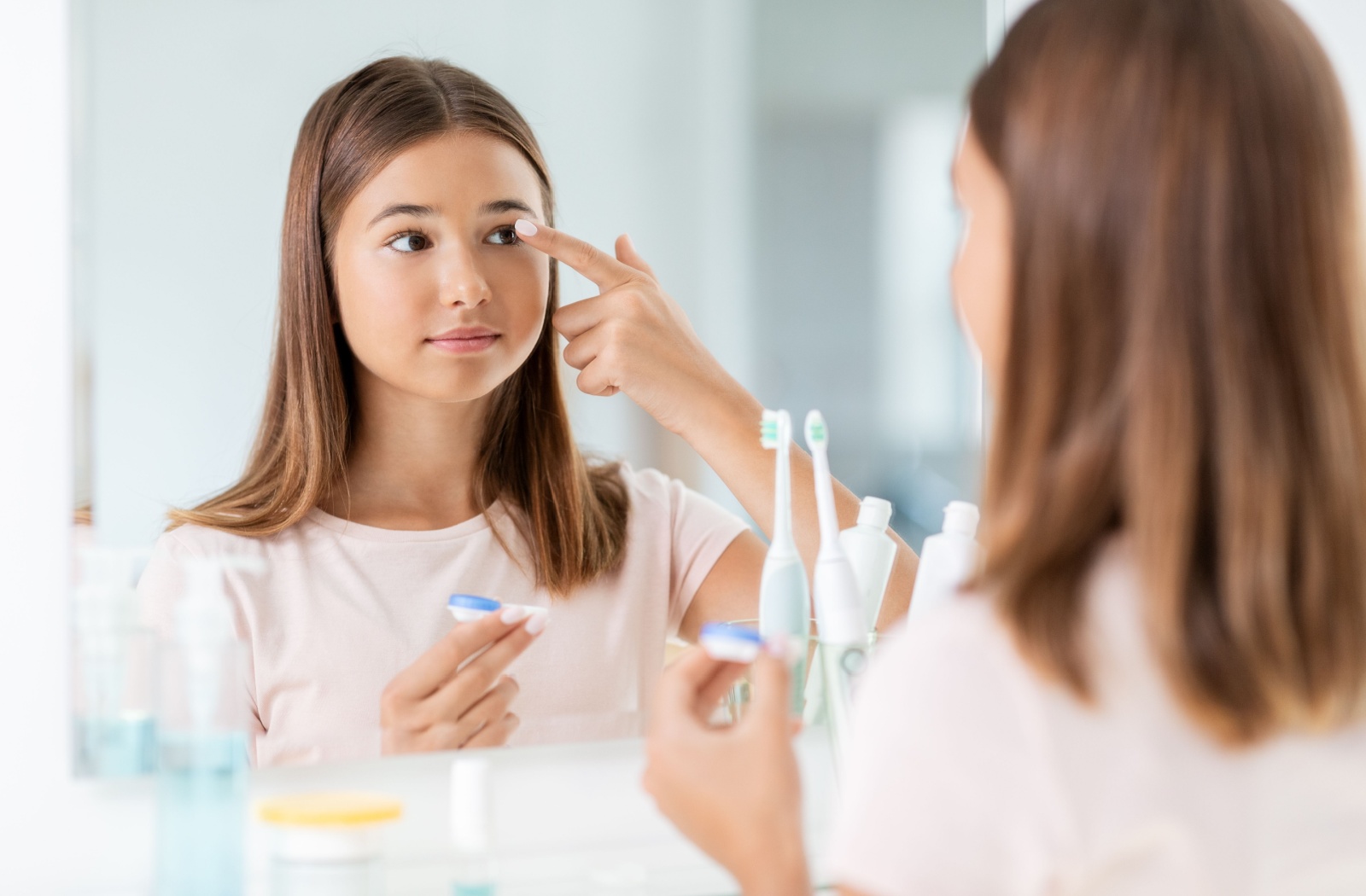 Girl putting in contact lens while looking in mirror.