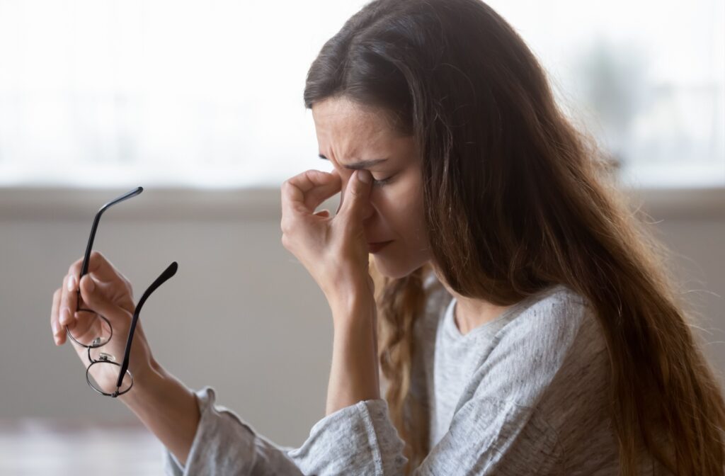 A person holding glasses in one hand while rubbing their eyes with the other due to the irritating symptoms of dry eye.